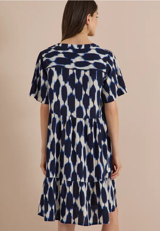 Frau von hinten in einem kurzärmligen, blau-weißen, gemusterten Kleid mit Stufensaum.