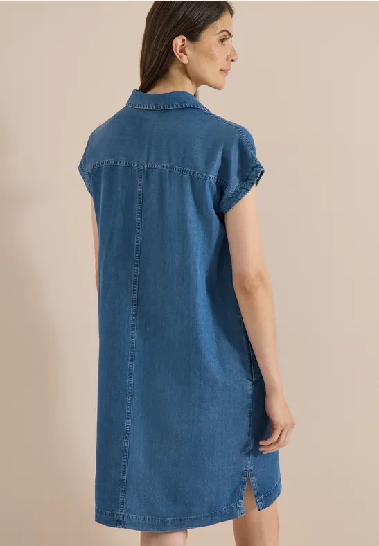 Frau von hinten in locker sitzendem Jeans-Hemdkleid mit kurzen Ärmeln vor neutralem Hintergrund.
