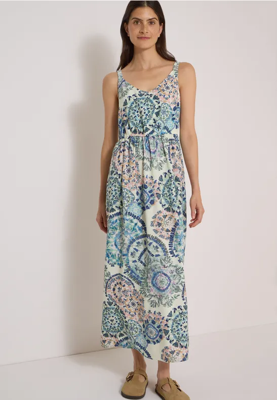 Femme en robe longue sans manches aux motifs mosaïque bleu-vert et fines bretelles, chaussures ouvertes.