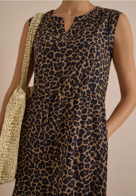 Vrouw in mouwloze blauw-bruin luipaardjurk met V-hals en strooien tas.