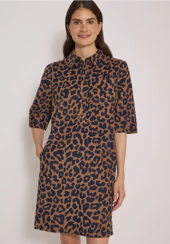 Eine Frau trägt ein knielanges Kleid mit halblangen Ärmeln, braun-schwarzem Leopardenmuster und seitlichen Taschen.