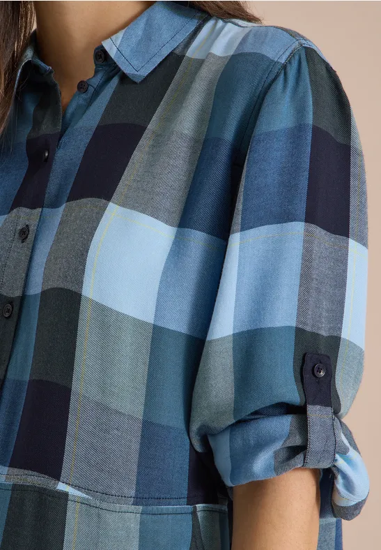 Gros plan d’une chemise à carreaux bleus avec des manches retroussées.