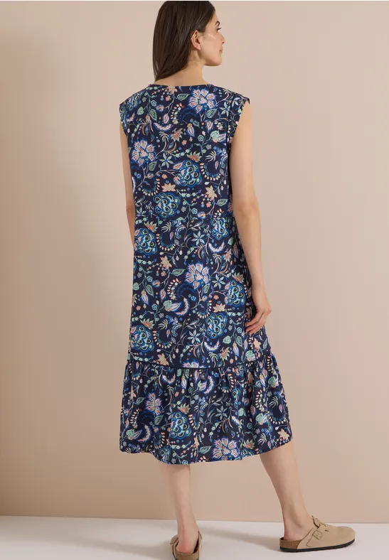 Rückenansicht einer Frau im ärmellosen Midikleid mit blauem Paisley- und Blumenmuster.