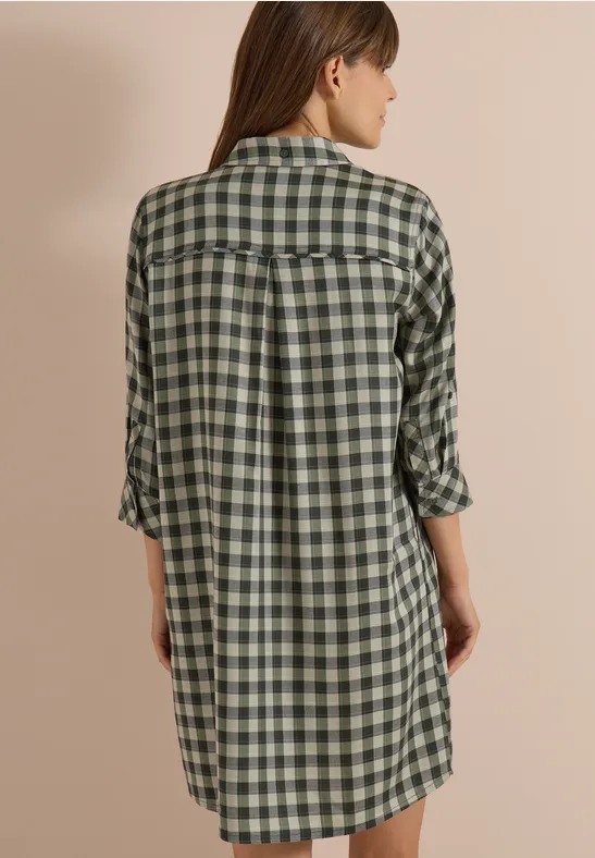 Vue arrière d’une femme portant une robe-chemise à carreaux verts ample.