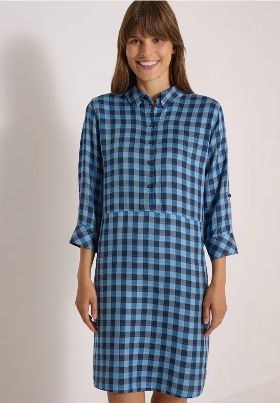 Eine lächelnde Frau trägt ein blau kariertes Hemdkleid mit 3/4-Ärmeln und Kragen.