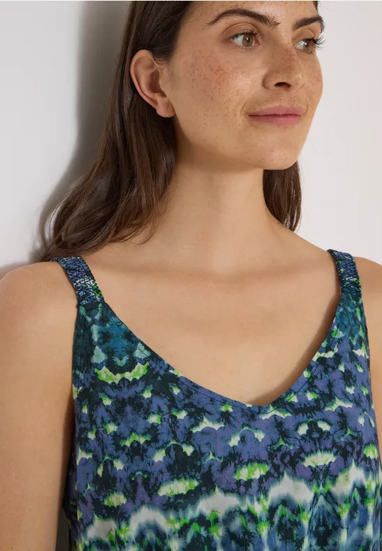 Femme porte un haut sans manches à motif abstrait bleu et vert.