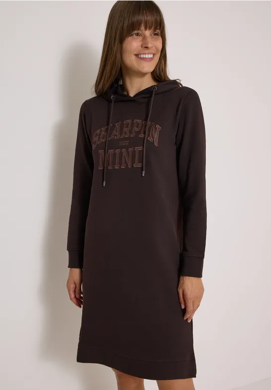 Vrouw glimlacht in een bruine hoodie-jurk met capuchon en print.