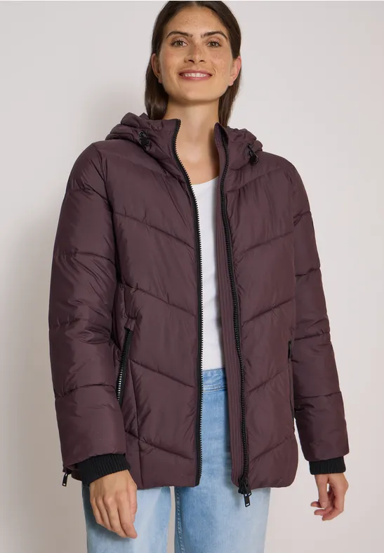 Frau in violettem, gepolstertem Winterparka mit Kapuze lächelt freundlich.
