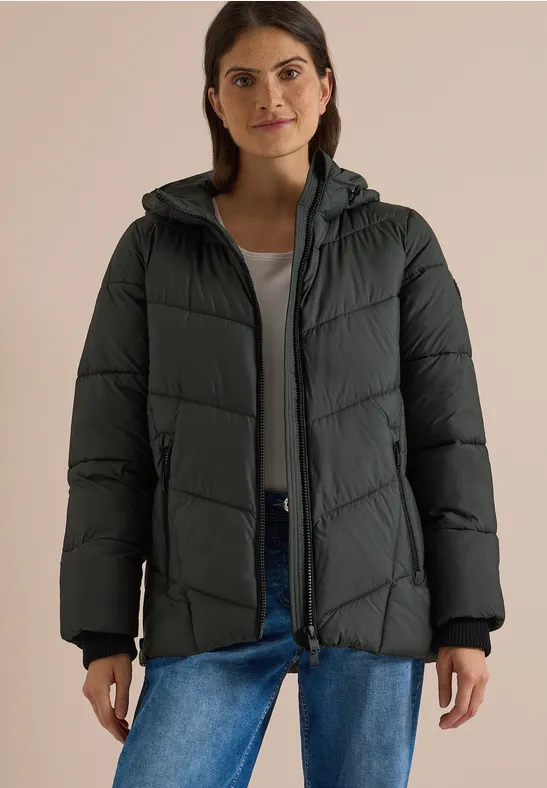 Frau trägt schwarze, wattierte Kapuzenjacke über grauem Shirt und blauen Jeans.