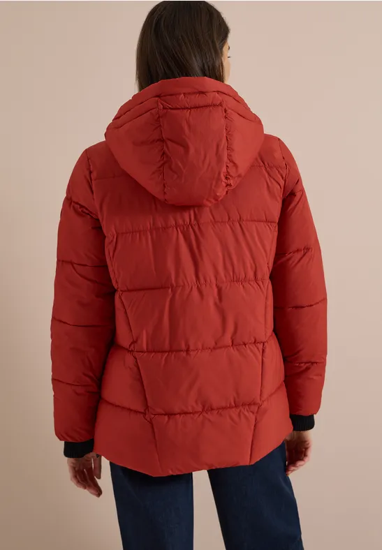 Rückenansicht einer Person mit roter gesteppter Jacke und Kapuze, kombiniert mit blauen Jeans.