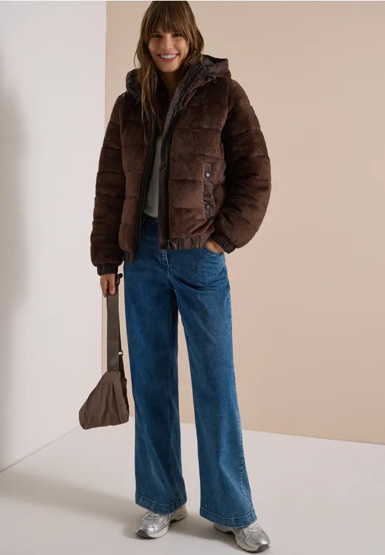 Frau in brauner Steppjacke, grauem Hoodie, weiten blauen Jeans, silbernen Sneakern und taupefarbener Tasche.