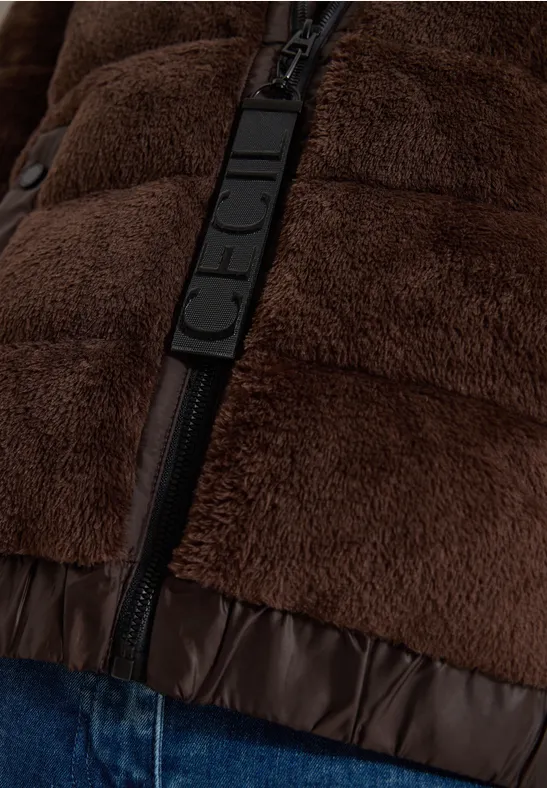 Nahaufnahme einer braunen, flauschigen Jacke mit schwarzem Reißverschluss und Zierlasche über Jeans.