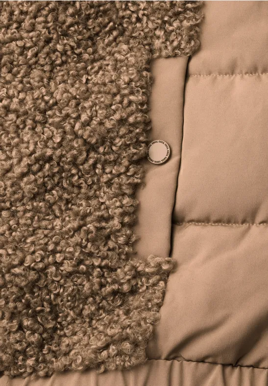 Gros plan d’une veste avec peau lainée à gauche, tissu matelassé à droite et bouton métallique au centre.