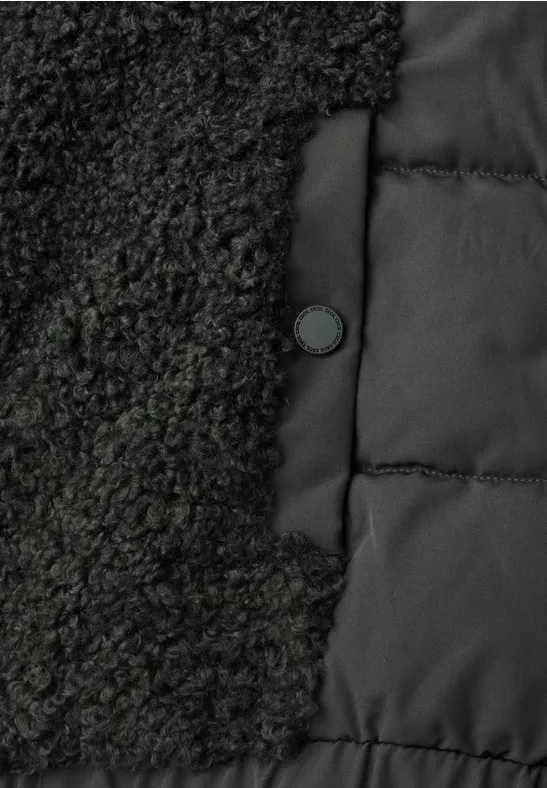 Gros plan d’une veste noire associant tissu polaire et matelassé avec un bouton-pression.