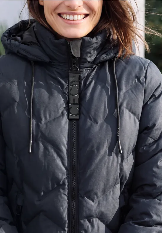 Eine Frau trägt eine schwarze gesteppte Winterjacke mit Kapuze und Reißverschluss.