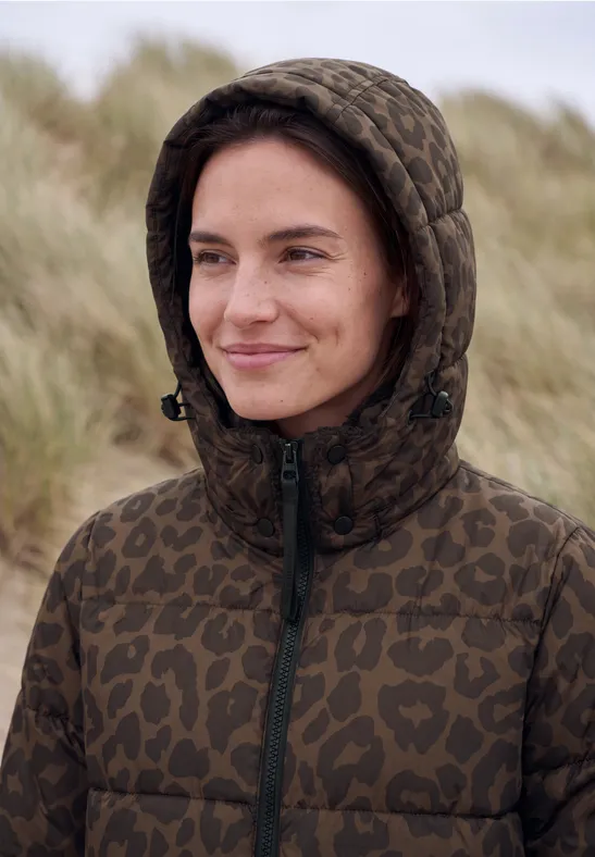 Eine lächelnde Frau in camouflage Steppjacke mit Kapuze vor Dünen
