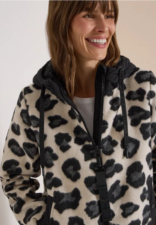 Lächelnde Frau in beigem Fleece-Hoodie mit schwarzem Leopardenmuster.