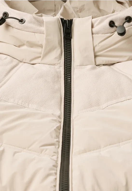 Nahaufnahme einer cremefarbenen, gesteppte Winterjacke mit Reißverschluss und Kordelzug am Kragen.