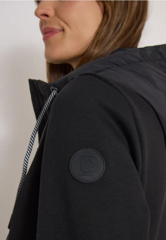 Femme de profil portant une veste à capuche noire sur un pull à manches longues