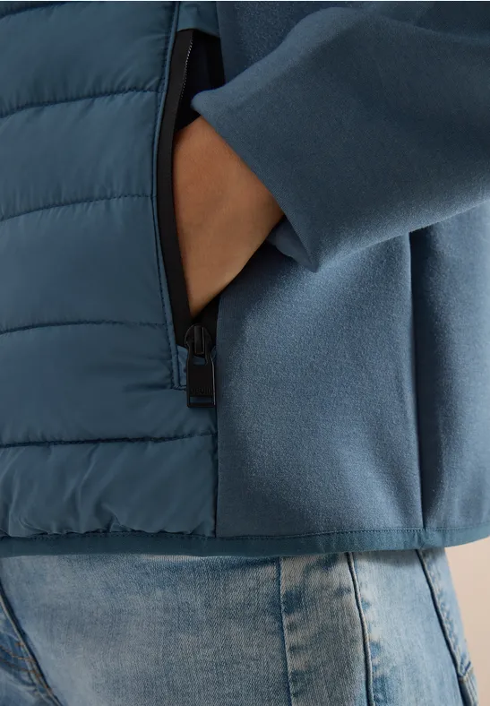 Hand steckt in der Reißverschlusstasche einer zweifarbigen blauen Jacke über Jeans.