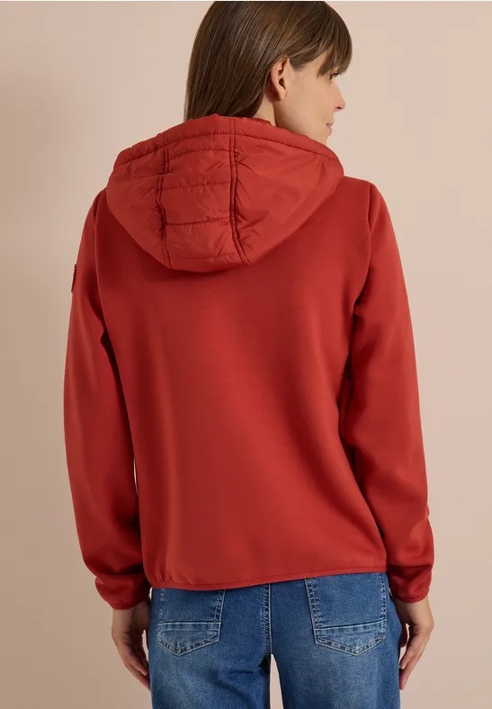 Rückansicht einer Frau in rotem Kapuzenpullover mit gesteppter Kapuze und Jeans.