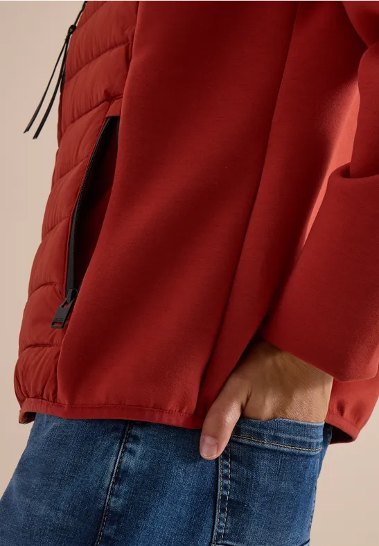Oberkörper mit roter Jacke und Hand in Jeans-Tasche, seitliche Reißverschlusstasche sichtbar.