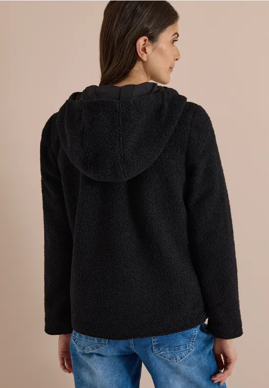 Frau von hinten in schwarzer, flauschiger Kapuzenjacke und blauen Jeans