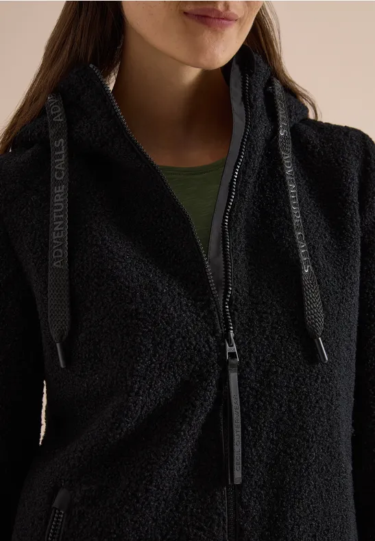 Nahaufnahme einer Frau in schwarzem Fleece-Jacke mit Reißverschluss und grünem Shirt.