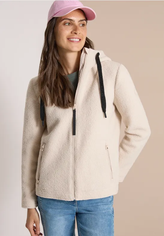 Eine lächelnde Frau mit rosa Baseballcap und kremfarbener Fleecejacke.