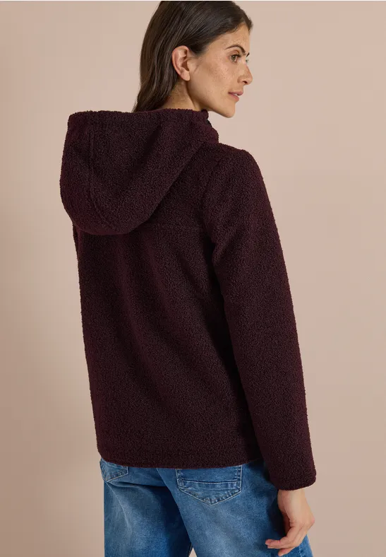 Frau im Profil, trägt eine burgunderrote Teddy-Fleecejacke mit Kapuze und Jeans.