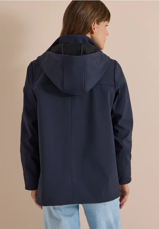 Une personne vue de dos porte une veste bleu marine à capuche devant un fond beige.