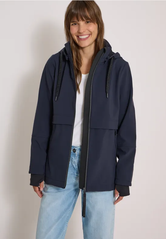 Femme en jean et tee-shirt blanc souriante, portant une veste à capuche bleu marine.