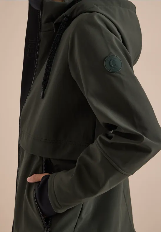 Parka softshell vert foncé à capuche, poche frontale et écusson logo sur la manche.