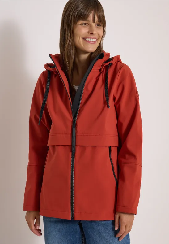 Lächelnde Frau trägt roten Outdoor-Parka mit Kapuze und Reißverschlüssen.