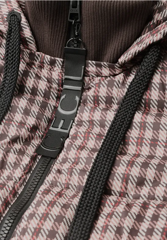 Nahaufnahme einer Jacke mit braun-weißem Hahnentritt-Muster, schwarzem Reißverschluss und Kordeln.