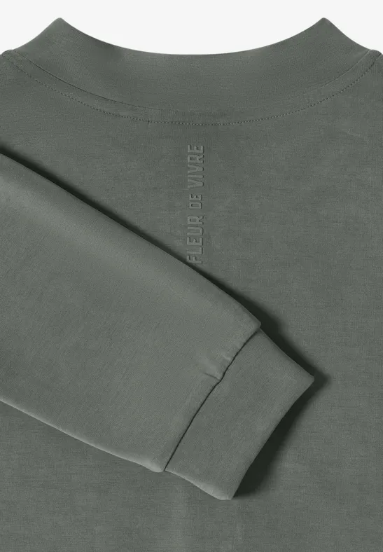 Olivgrüner Sweatshirt-Oberteil mit gefaltetem Ärmel auf hellem Hintergrund