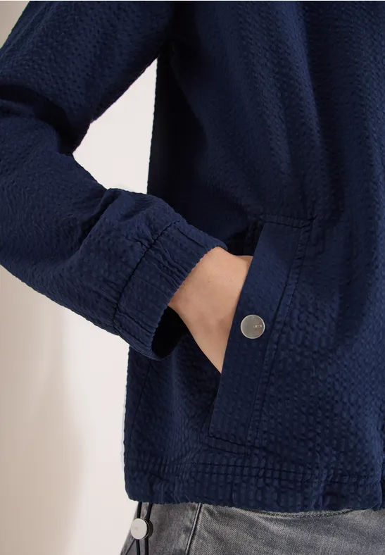 Dunkelblaue, texturierte Jacke mit verdeckter Tasche, Hand in der Seitentasche und Metallknopf