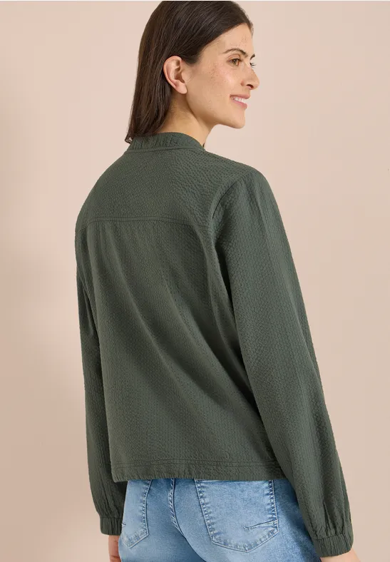 Achteraanzicht van een persoon in een groene blouse en blauwe jeans tegen een neutrale achtergrond.
