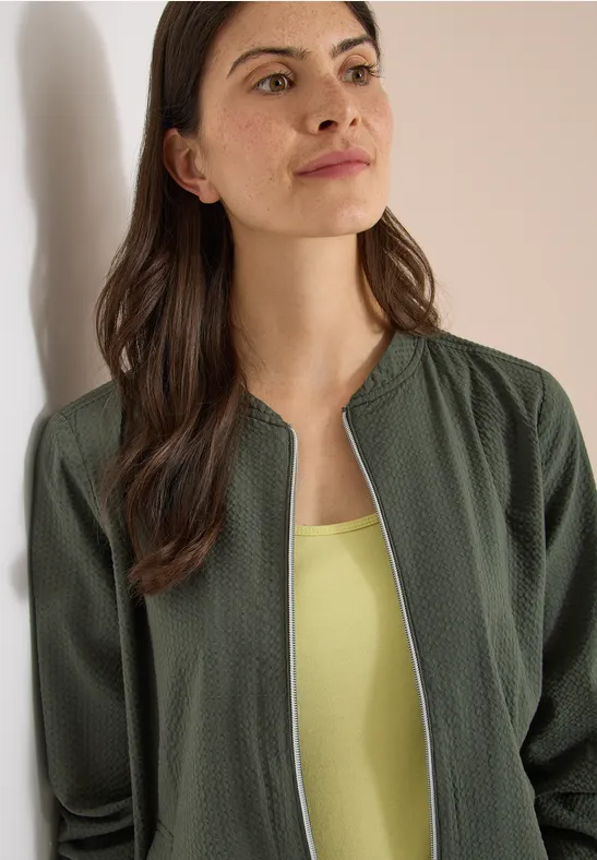 Vrouw met een olijfgroene, ritssluiting vest over een lichtgroen hemd.