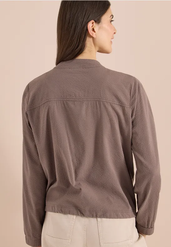 Vrouw van achteren in een taupekleurig jack voor een neutrale achtergrond.