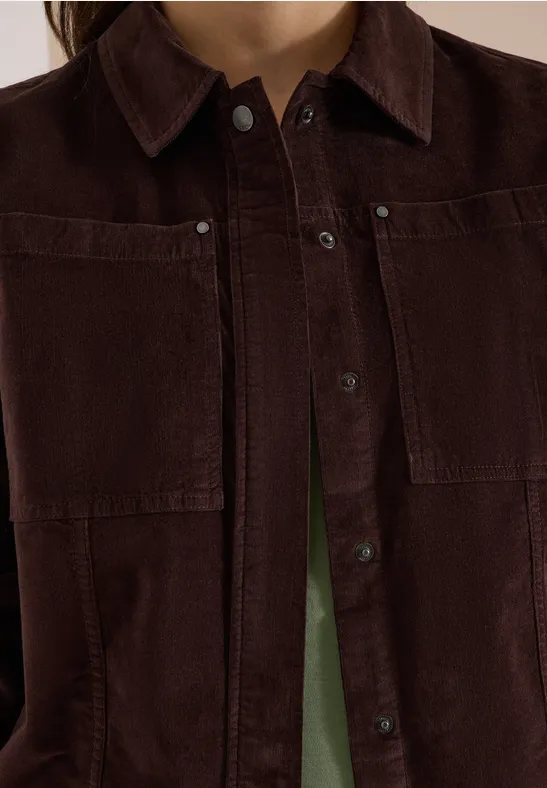 Veste en velours côtelé marron foncé avec poches avant et boutons, chemise verte en-dessous.