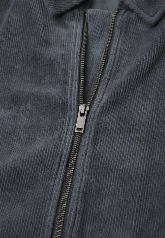 Nahaufnahme eines grauen Cord-Jackenreißverschlusses.