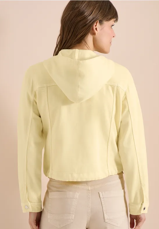 Frau von hinten in hellgelber Kapuzenbluse und beigen Hosen.