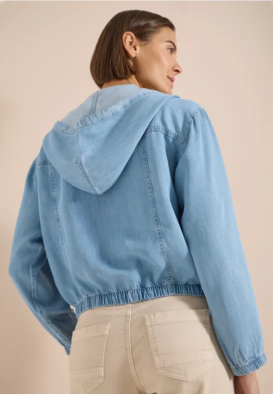 Femme vue de dos portant une veste en jean bleu clair à capuche.