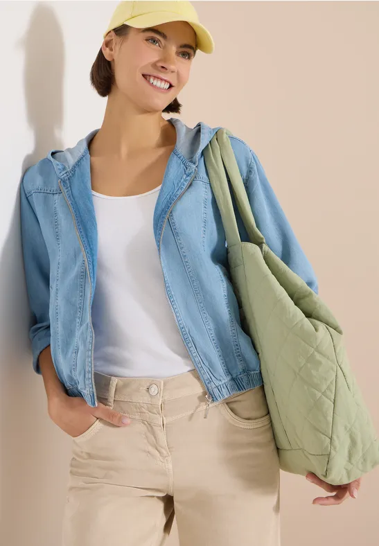 Personne porte un débardeur blanc, une veste en jean bleu clair, un pantalon beige et un sac matelassé vert.