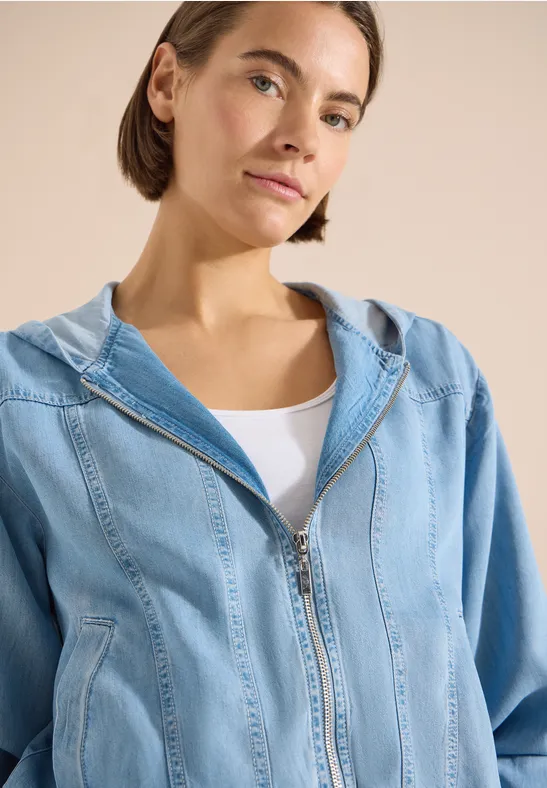 Femme portant un hoodie en jean bleu clair avec fermeture éclair et débardeur blanc, visage flouté.