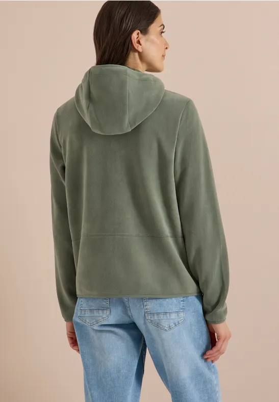 Vrouw van achteren in groen met capuchon en spijkerbroek, kijkt iets opzij