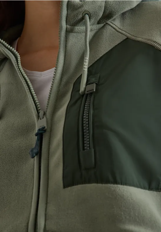 Close-up van een groene jas met rits en borstzak.
