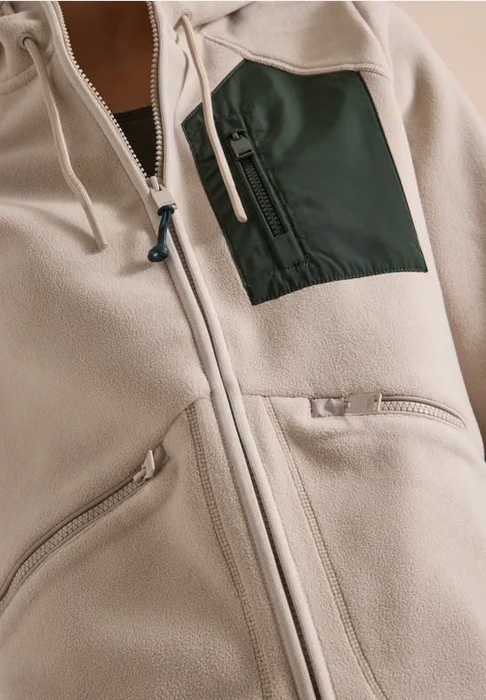 Nahaufnahme einer hellen Fleecejacke mit Reißverschluss und farblich abgesetzter Brusttasche.