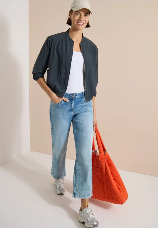 Femme portant une veste noire, un top blanc, un jean ample, des chaussures argentées et un grand sac rouge.